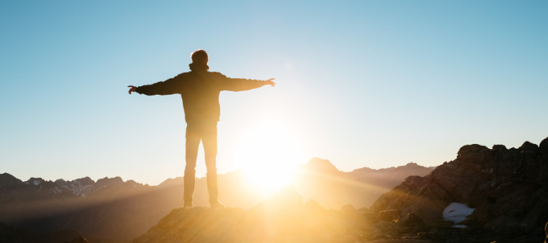 Silhouette of a man with arms outstretched, enjoying a mountaintop sunrise.