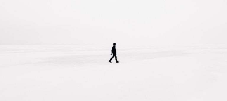 Person walking alone in a vast, white landscape.