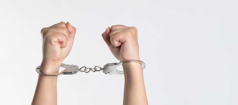 Close-up of hands cuffed together with metal handcuffs.