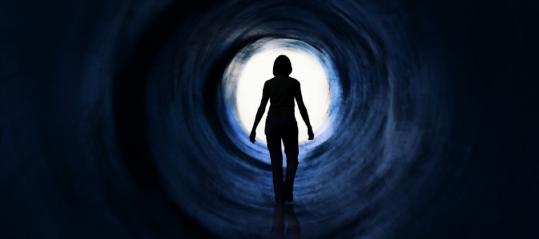 Silhouette of a woman walking toward a bright light at the end of a dark tunnel.