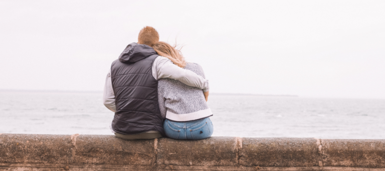 Couple embracing, looking out at the ocean.