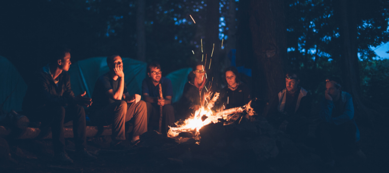 Group of friends gathered around a campfire at night, enjoying each other's company.