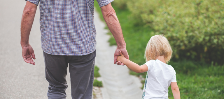 Grandfather and grandchild holding hands, walking outdoors.