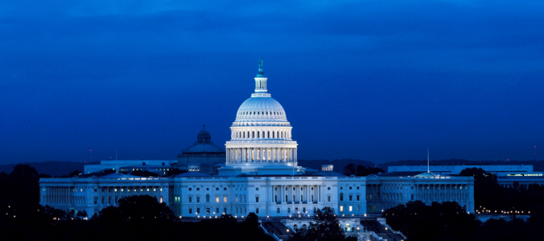 The US Capitol Building at night, illuminated against a dark blue sky.