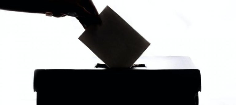 Hand dropping ballot into a ballot box. Voting process.