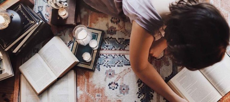 Woman reading books surrounded by candles and other books. Exploring science, philosophy, and theology.