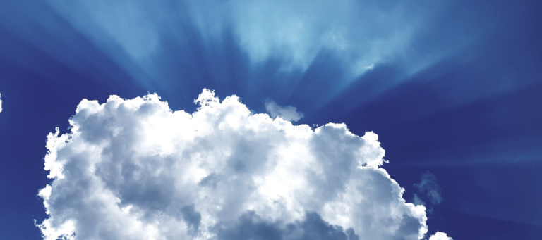Bright sunbeams shining through fluffy cumulus clouds in a deep blue sky.