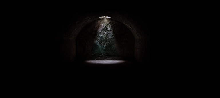 Light shining through a small opening in a dark, arched tunnel.