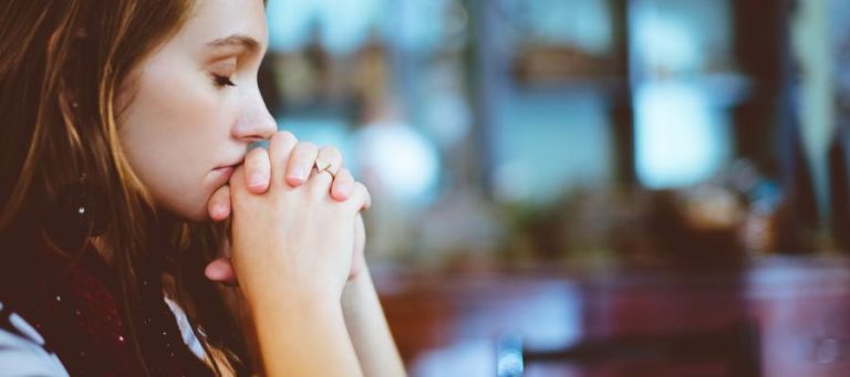 Thoughtful young woman with hands clasped, contemplating existence.