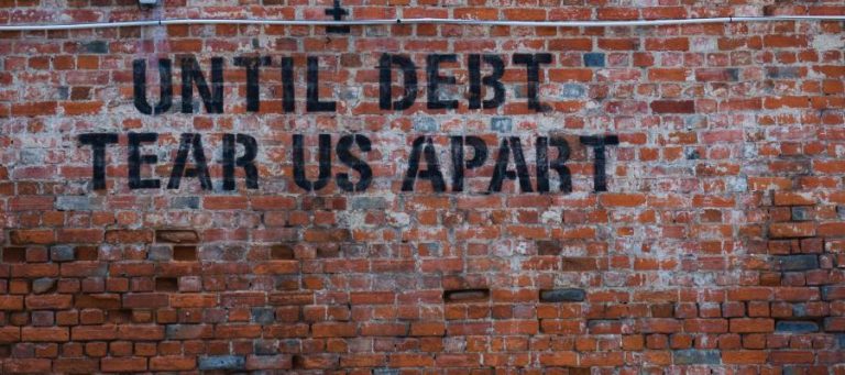 Brick wall with graffiti: "Until debt tear us apart.