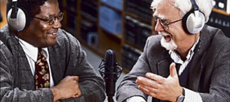 Two men wearing headphones discuss a topic during a radio broadcast.