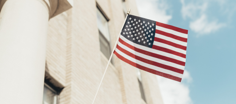American flag waving in front of a building. Dewey's Democracy.