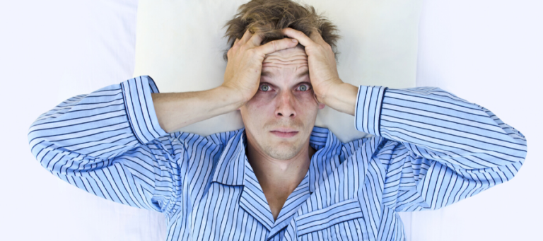 Frustrated man in pajamas lying in bed, hands on head.