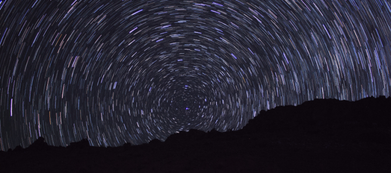 Star trails circling a dark mountain range at night.