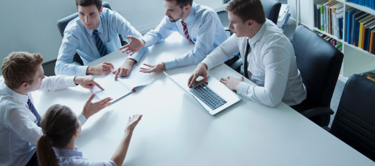 Business team collaborating around a table, discussing documents and using a laptop.