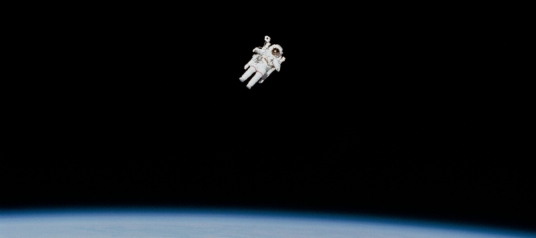 Astronaut performing spacewalk against black backdrop of space and Earth's horizon.