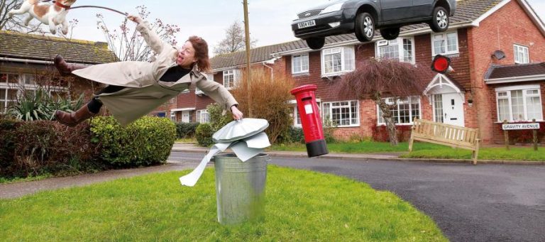 Woman flying through the air, dog on a leash, car and postbox floating; Gravity Avenue street sign.