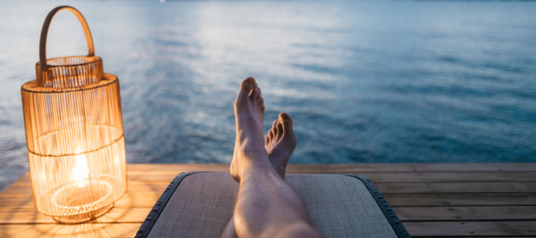 Person's feet up, relaxing by the water at sunset.