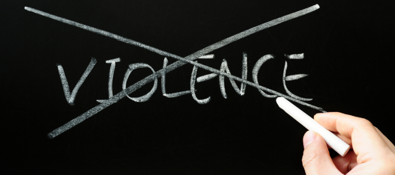 Chalkboard with the word "VIOLENCE" crossed out. A hand holds chalk, emphasizing the rejection of violence.