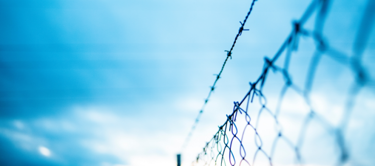 Barbed wire fence against a blue sky.