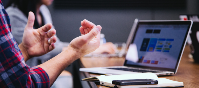 Person gesturing during a business meeting, laptop displaying data on the table.