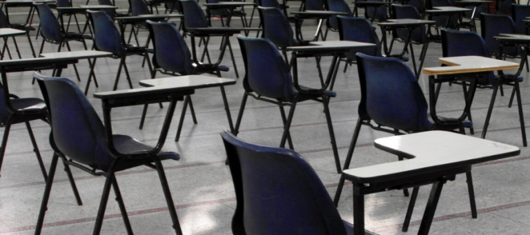 Rows of empty exam desks and chairs in an examination hall.