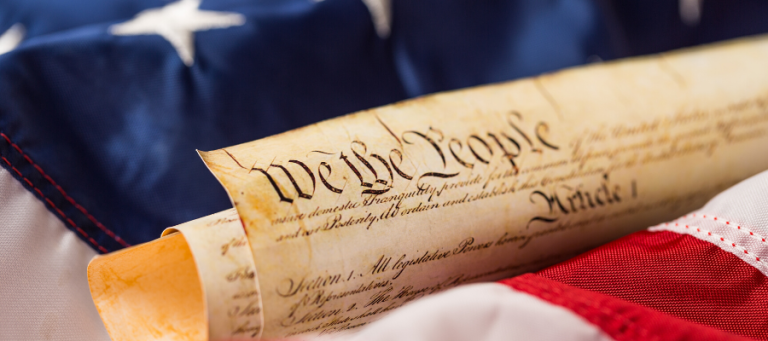 Close-up of the U.S. Constitution text, "We the People," on aged parchment resting on an American flag.