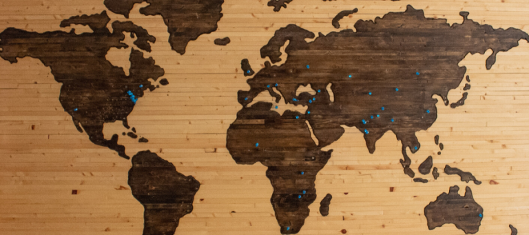 World map on wood with blue pins marking locations.