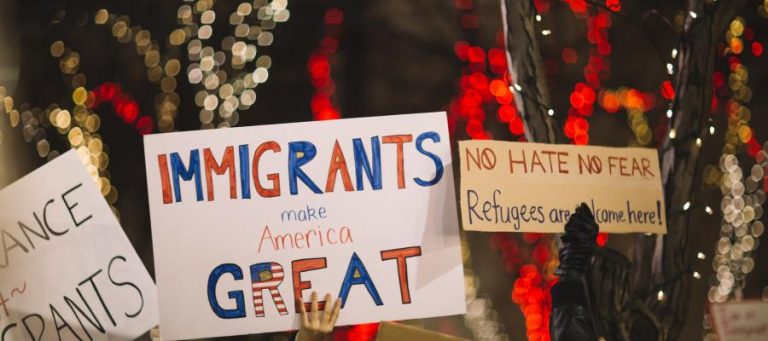 Protest signs reading "Immigrants make America Great" and "No Hate No Fear. Refugees are welcome here!