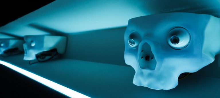 Row of stylized skull sculptures with glowing eyes, illuminated in blue light.