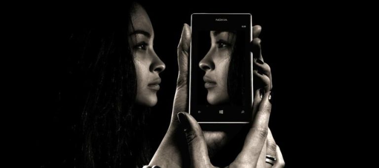 Woman holding phone displaying her reflection, exploring unconscious bias.