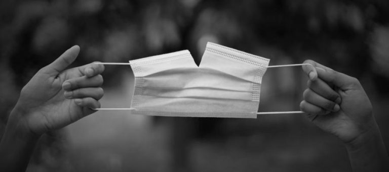 Torn face mask held by two hands, symbolizing the accessibility debate in the arts.