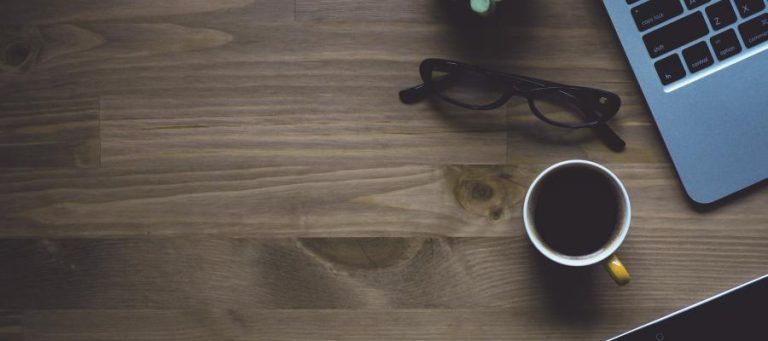 Laptop, coffee cup, eyeglasses on a wood desk
