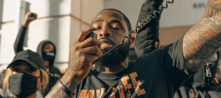 Man with tattoos speaking into a microphone at a protest.