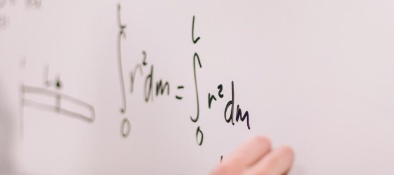 Close-up of a hand writing a math equation on a whiteboard; integral of r squared dm equals integral of r squared dm.