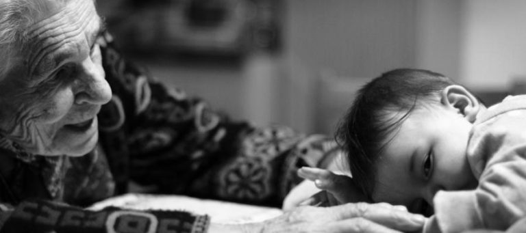 Elderly woman lovingly cradles a sleeping baby. Generational connection.