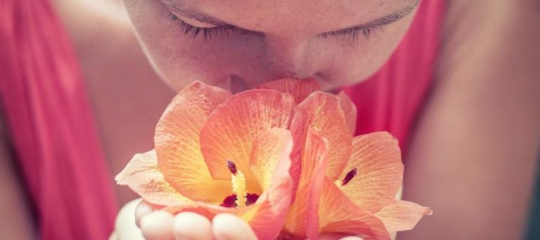Close-up of a woman smelling a vibrant orange flower.