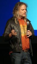 Man with long hair speaking at a conference