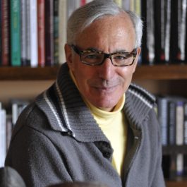 Portrait of a man wearing glasses, seated in front of bookshelves.