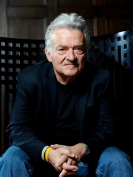 Portrait of older man with gray hair, wearing a black jacket and jeans.