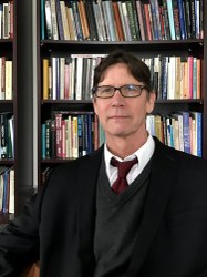 Portrait of a man in a suit, seated in front of bookshelves.
