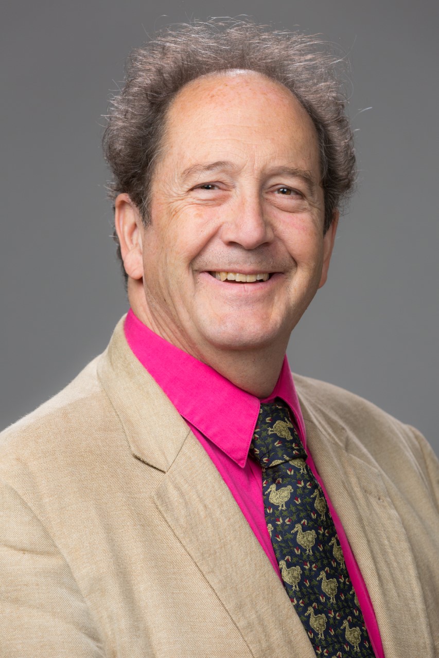 Smiling man in beige jacket and pink shirt, illustrating moral ambiguity.