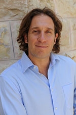 Headshot of a man with shoulder-length brown hair, wearing a light blue shirt.