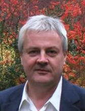 Headshot of a middle-aged man with short gray hair, wearing a dark blazer.