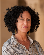 Headshot of a woman with dark, curly hair, wearing a patterned shirt.