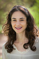 Headshot of a woman with dark curly hair, wearing a cream-colored top.