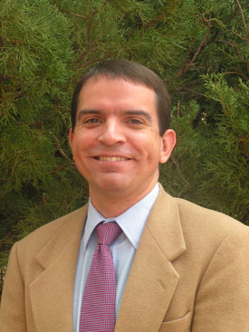 Headshot of a man in a tan suit and purple tie