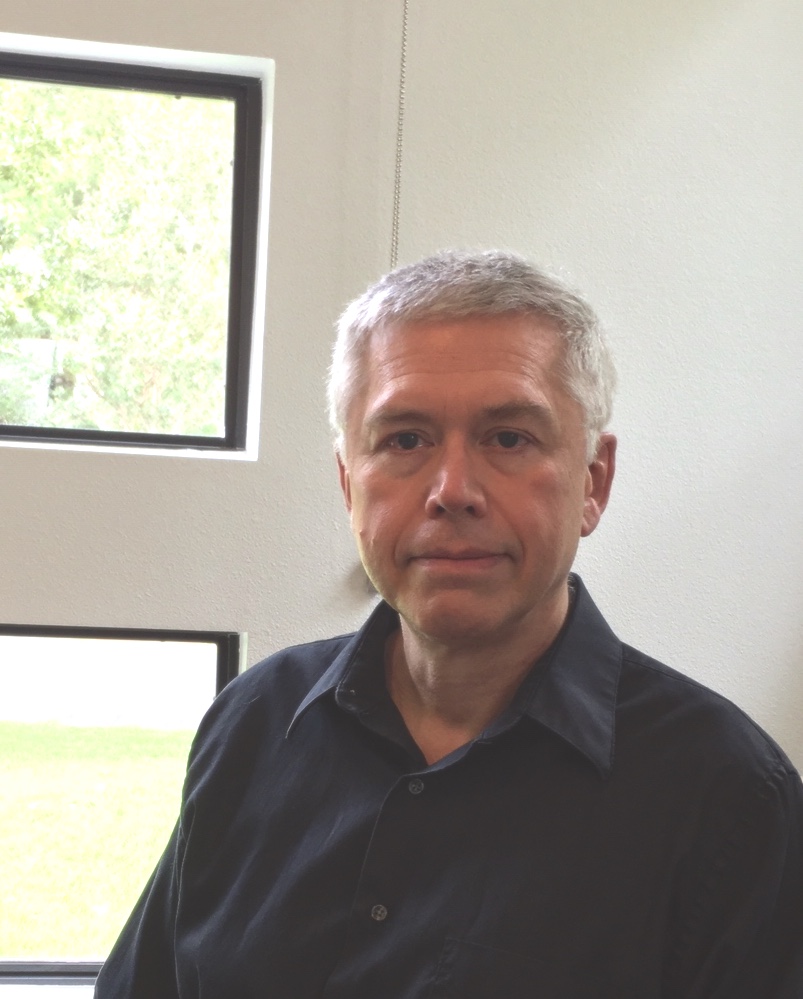 Headshot of a man with short gray hair, wearing a black collared shirt.
