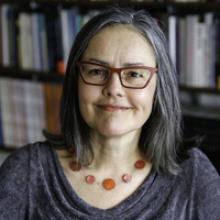 Portrait of a woman with gray hair and red glasses, wearing a necklace.