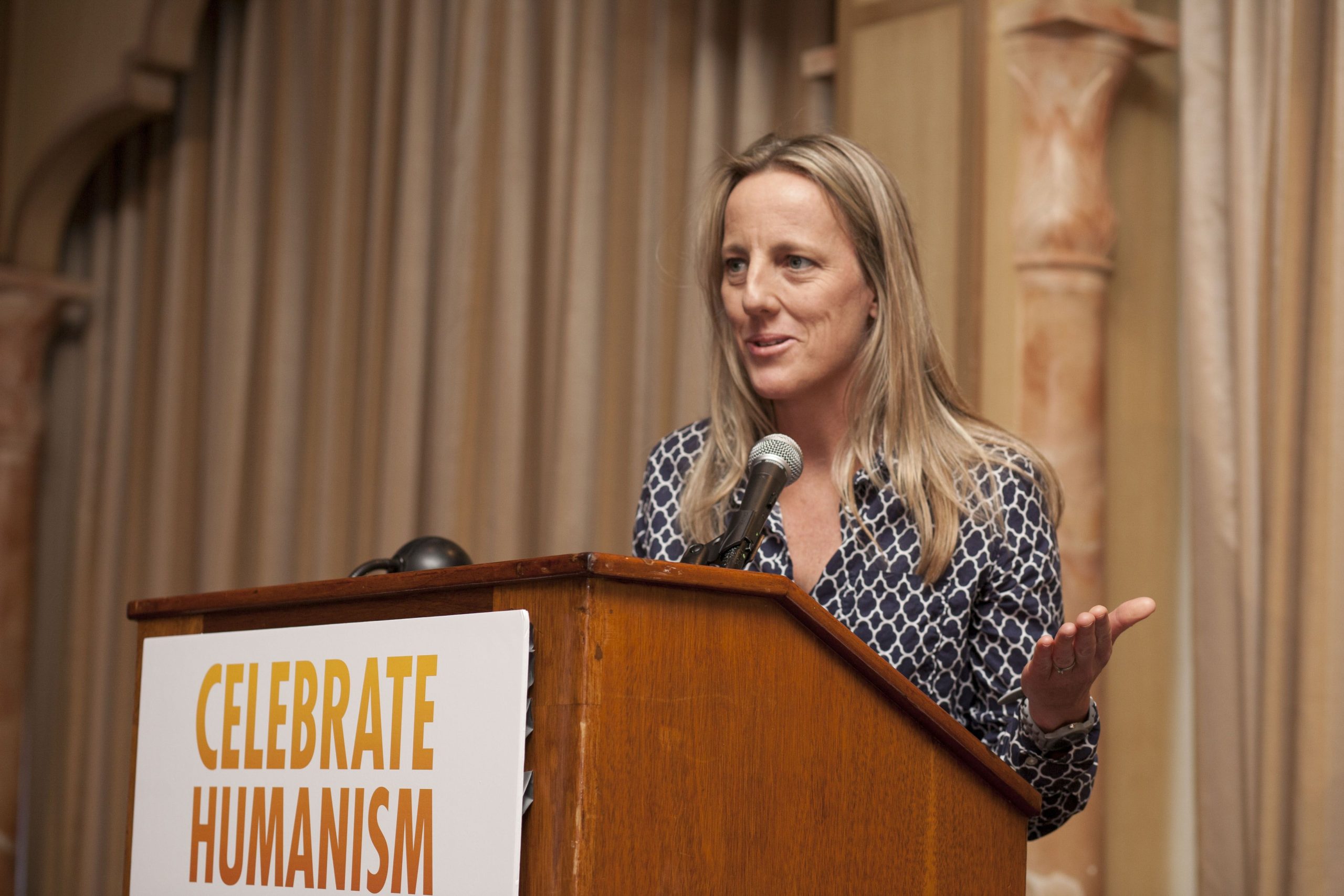 Woman speaking at a podium, "Celebrate Humanism" sign visible.